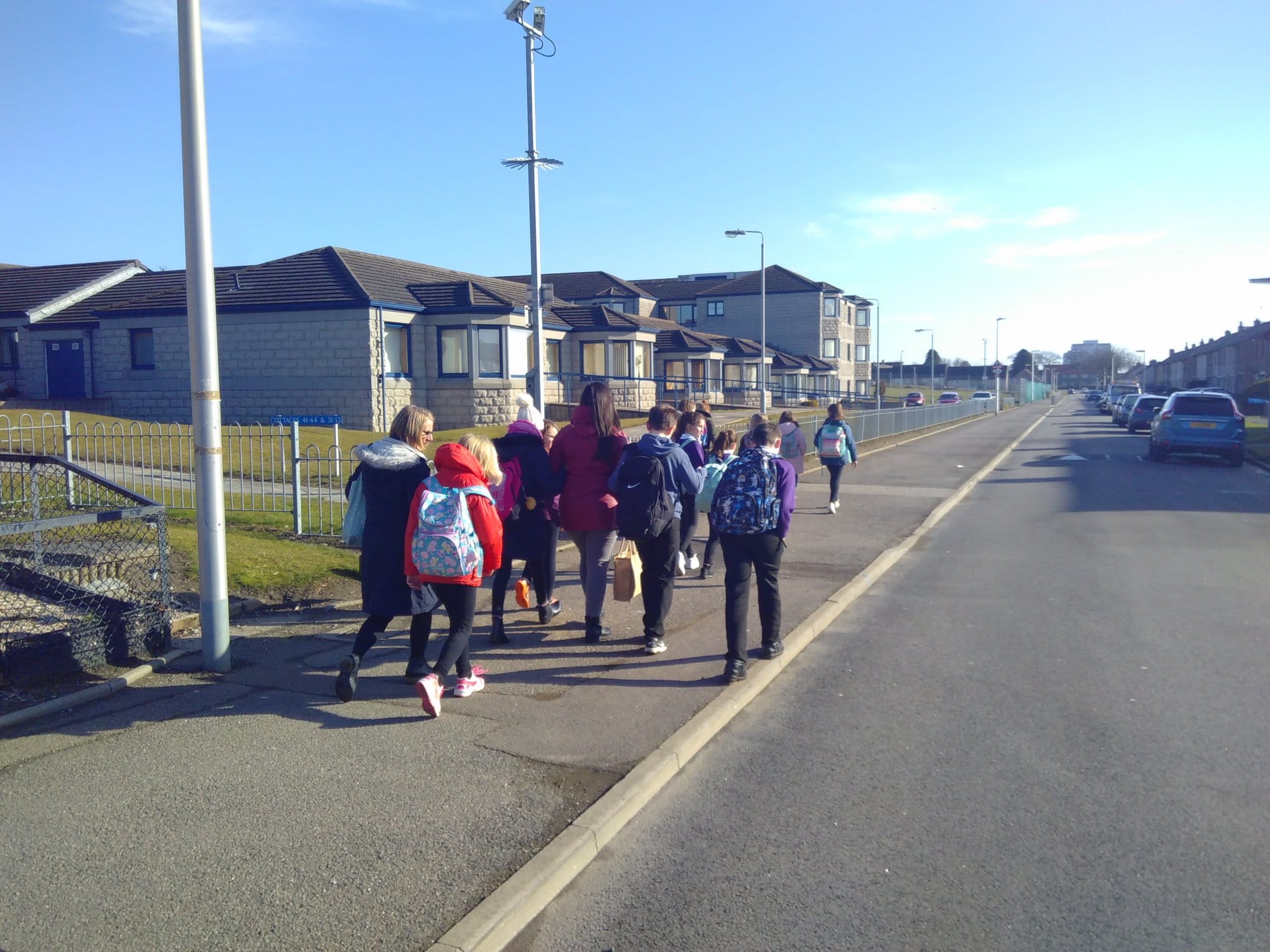 Group of children and adults walking along a residential street.