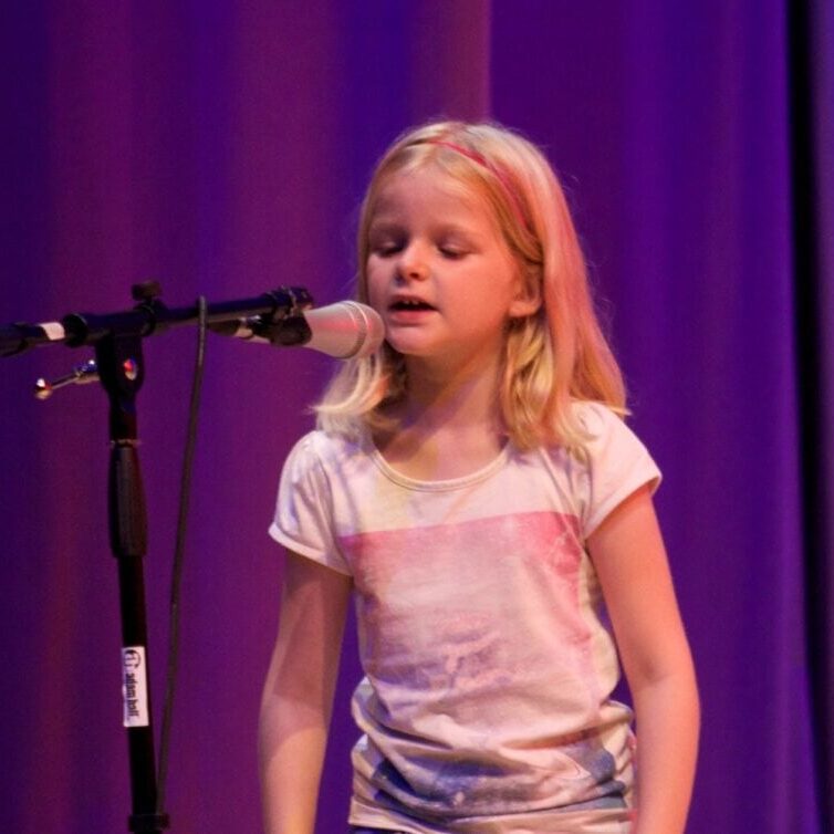 Young girl performing on stage with microphone, showcasing confidence and voice.