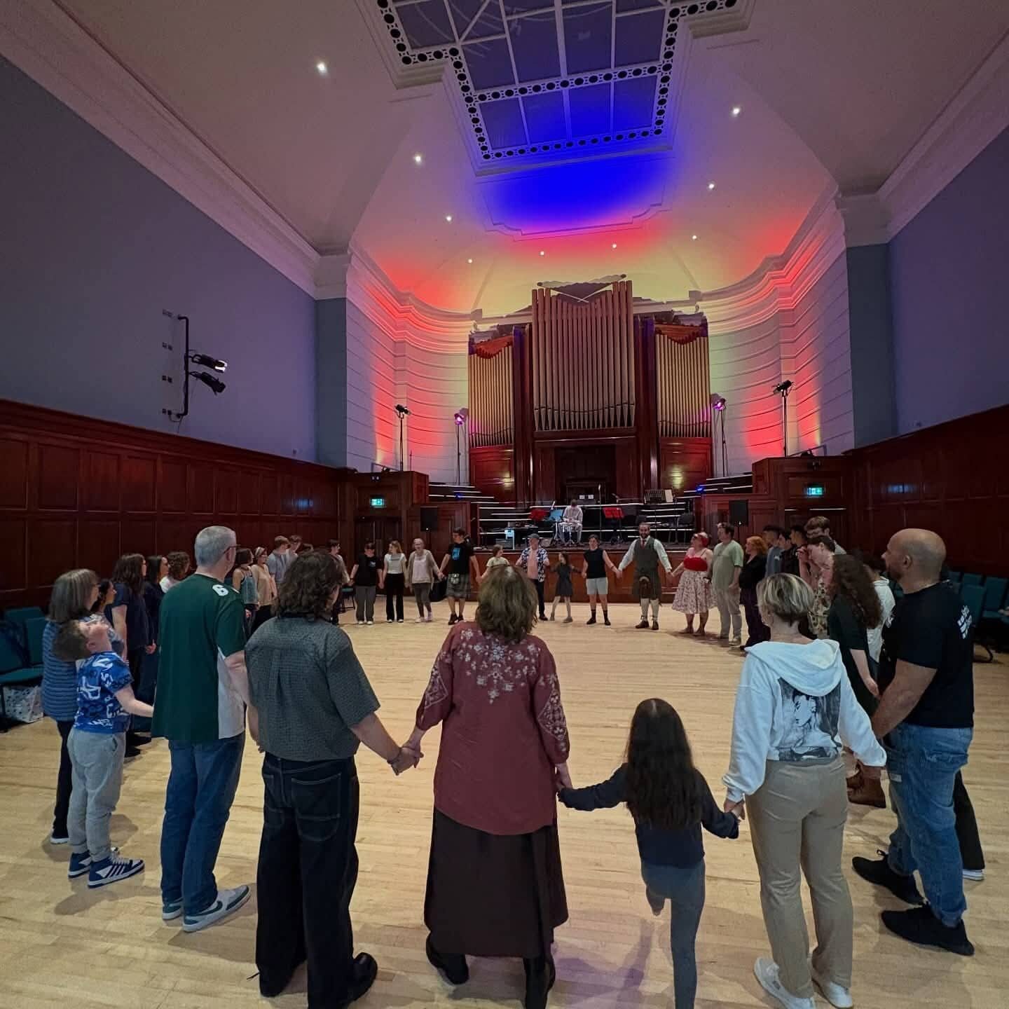 Diverse group holding hands in a circle at ACE Voices event in a concert hall.